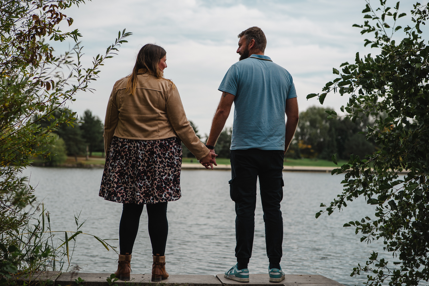 couple qui se tient la main et se regarde face au lac dans un parc