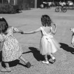 3 petites filles de dos en robes de ceremonie qui courent en se tenant la main devant mairie