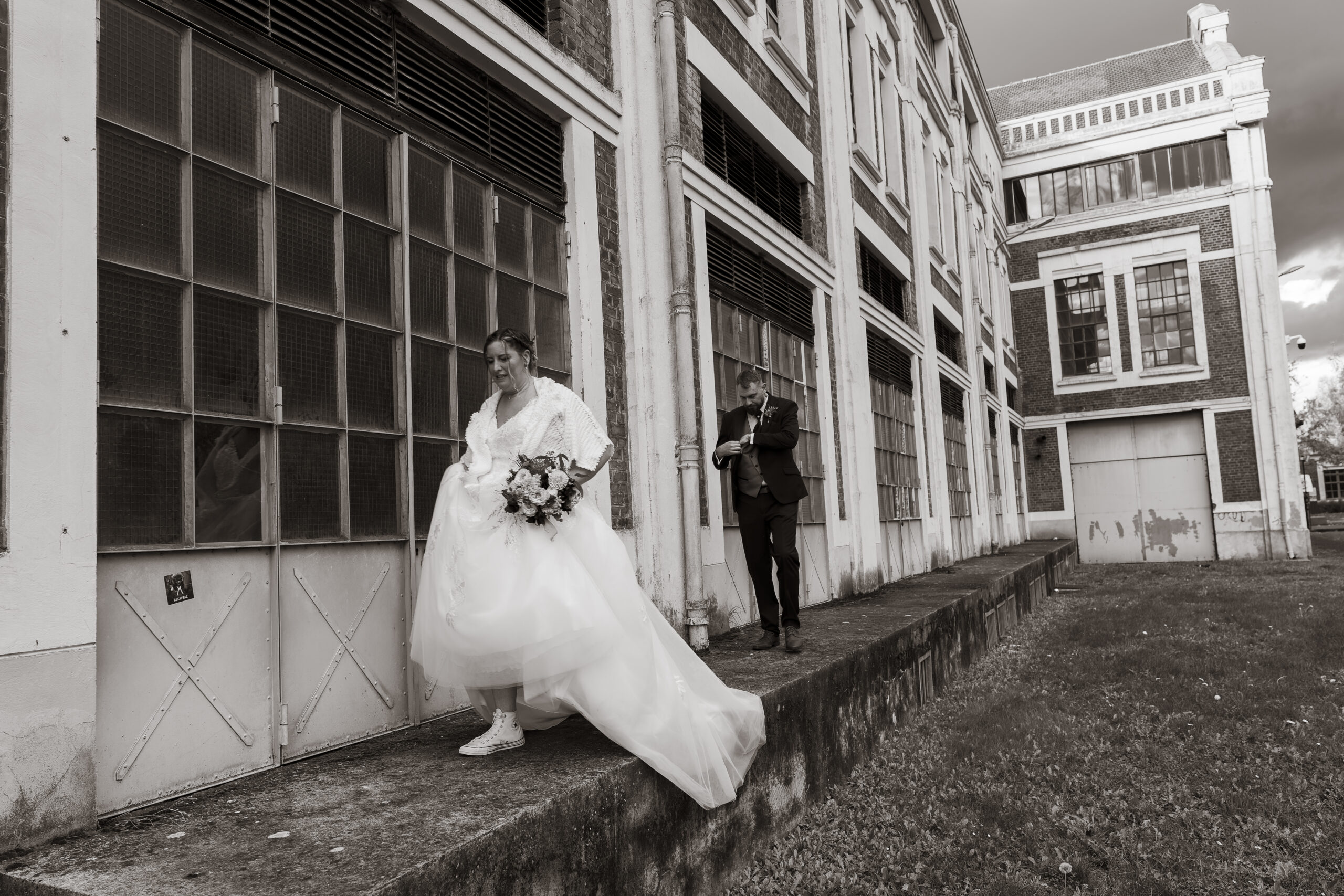 photo de couple marié dans un site minier qui marchent main devant batiment industriel