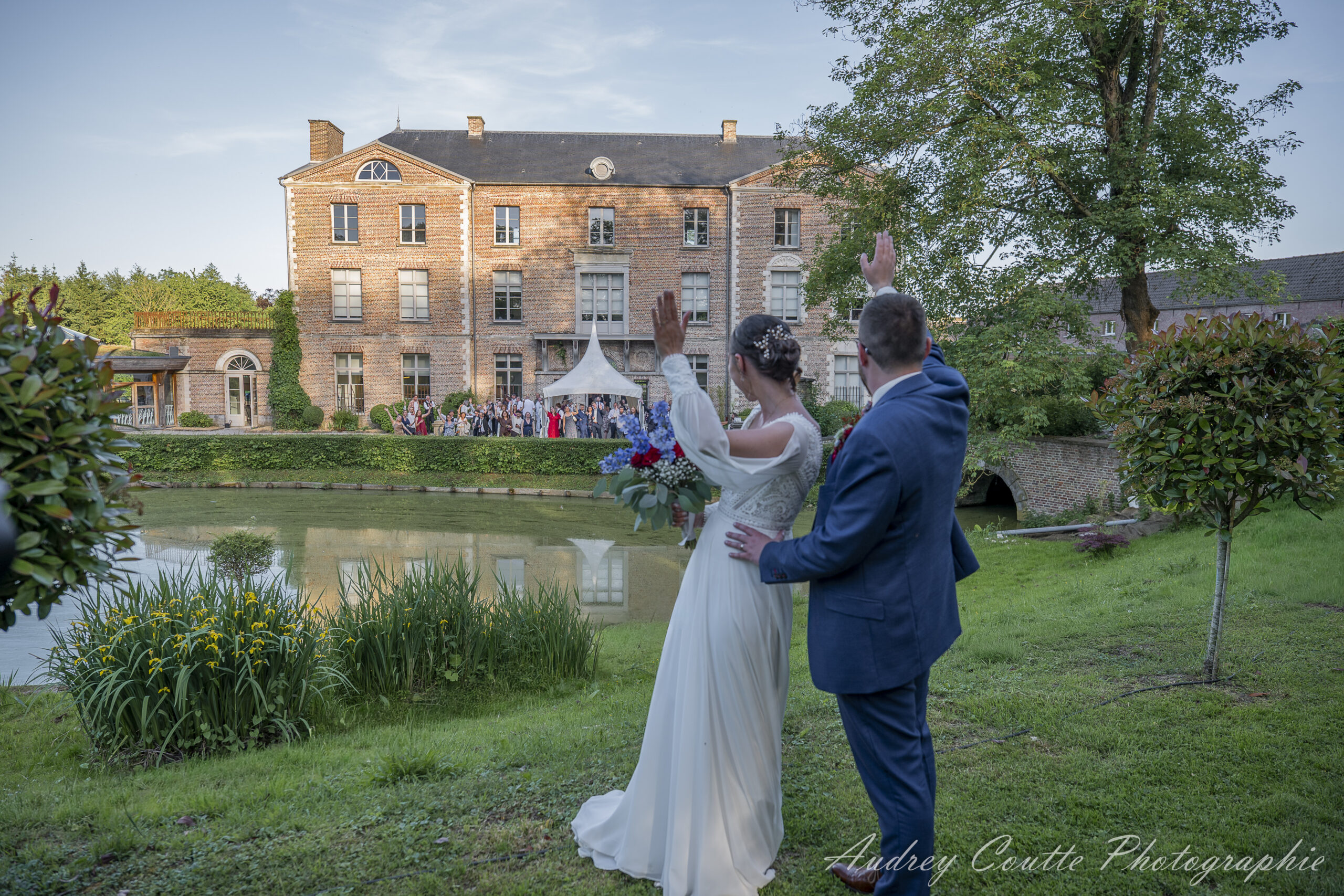 Mariage Manon & Lewis au Chateau de Morbecque, photo de couple dans le parc du château les maries font signe aux invités