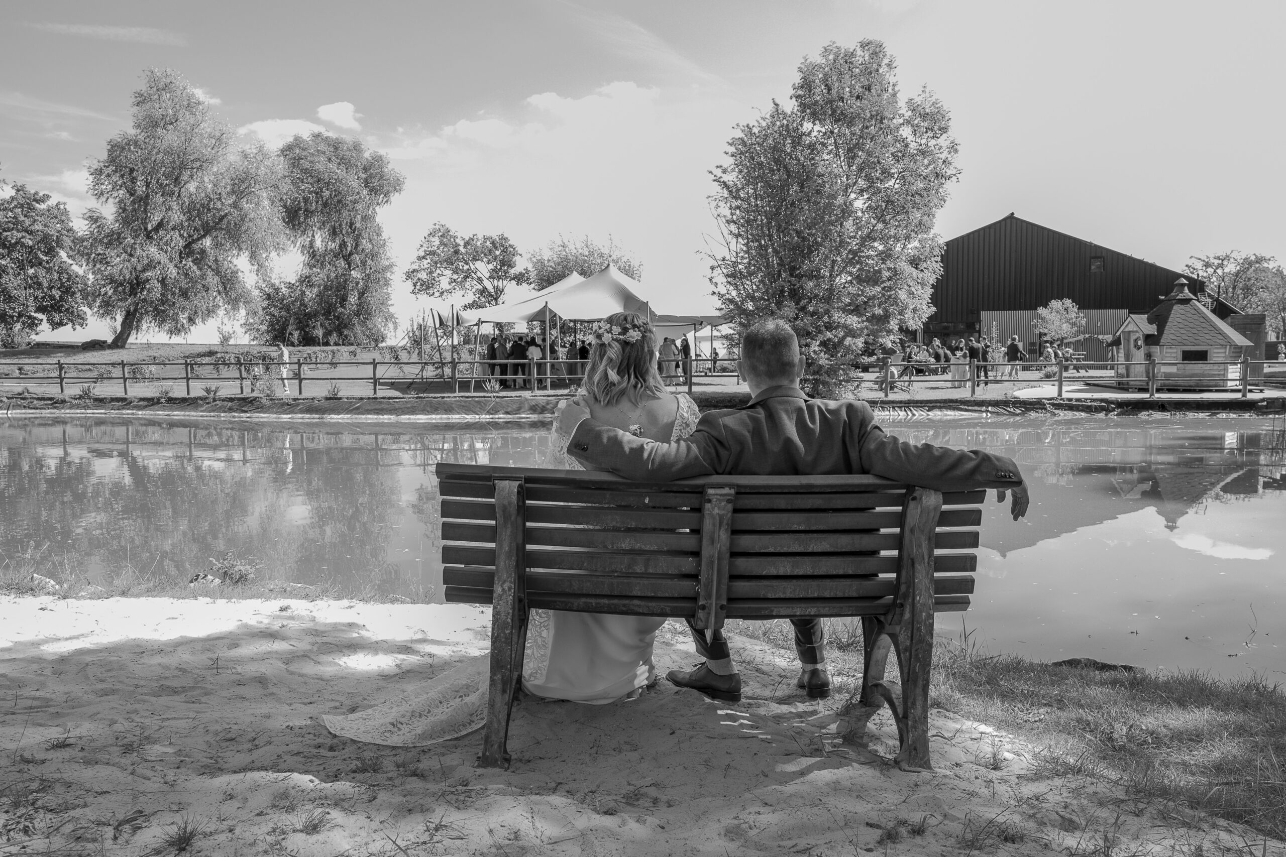 les maries assis sur un banc devant l'étang et leurs invités pendant le cocktail